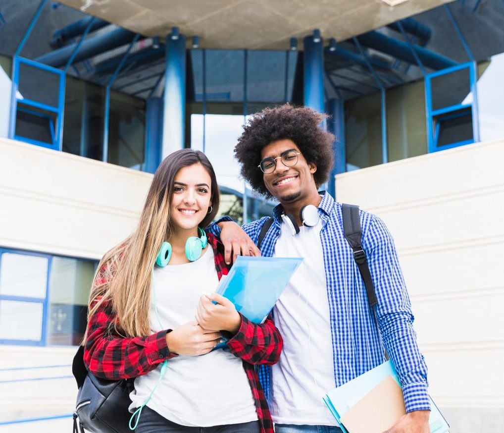 smiling portrait young couple holding books hand standing front university building looking camera_23 2148093382 e1711793523912